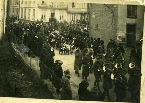 Front of poscard. Sepia image of soldiers and people on the street.