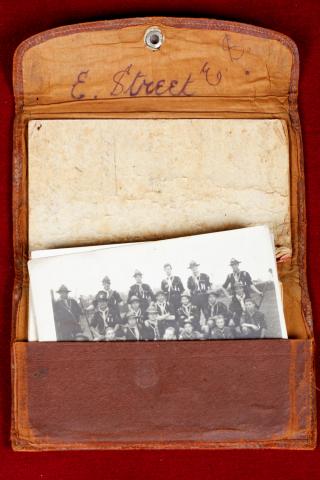 Worn leather-like wallet with a black and white photograph of men in uniform inside.