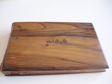 Image depicts book with a wooden cover, with an inscription in Hebrew.