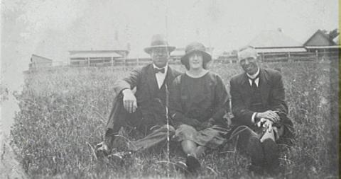 Black and white photo of three people posing, outdoors. 
